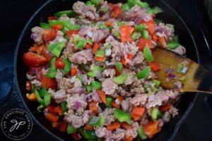 Healthy Turkey Sloppy Joes ingredients in a cast iron skillet with a wooden spoon.