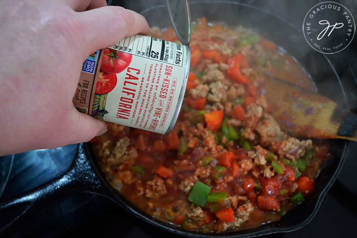 Adding tomato sauce to Healthy Turkey Sloppy Joes filling in a skillet.