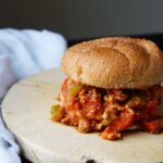 A single Healthy Turkey Sloppy Joe sits on two cutting boards with a white towel laying next to them.