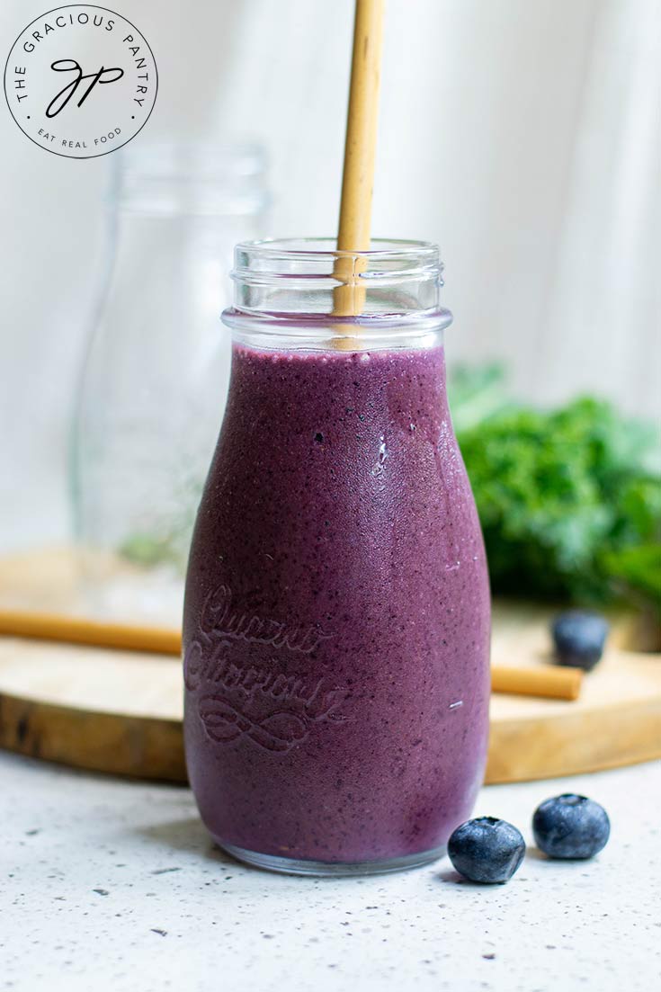 A single glass milk jug sits filled with Kale Blueberry Smoothie. A straw sits in the jar and smoothie as well.