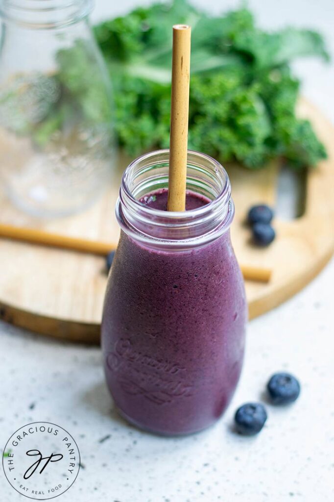 A single, small, milk jug sits filled with Kale Blueberry Smoothie. It also holds a brown straw.
