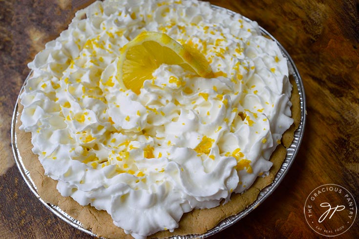 A finished, whole, lemon cream pie garnished with a single lemon slice in the middle.