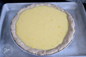 Lemon cream pie filling sitting in a pre-baked pie crust. The pie dish sits on a baking pan for stability.