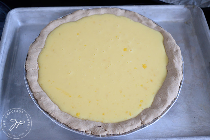Lemon cream pie filling sitting in a pre-baked pie crust. The pie dish sits on a baking pan for stability.