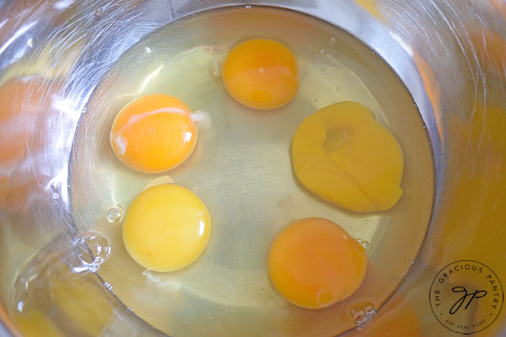 Five cracked eggs sit, unmixed, in a mixing bowl.