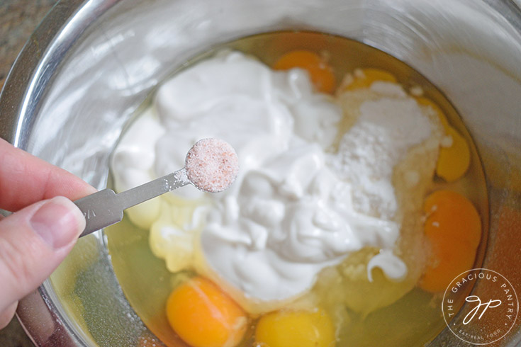 Adding salt to lemon cream pie filling ingredients sitting in a mixing bowl.