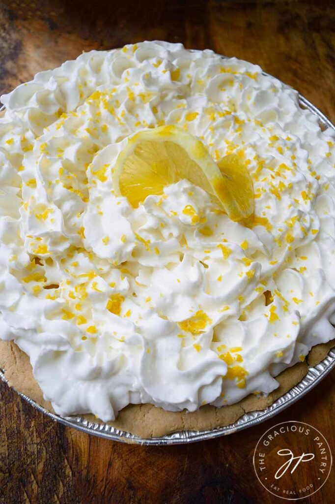 An overhead view looking down on a whole lemon cream pie garnished with fresh lemon zest and a single lemon slice in the middle, artfully arranged.