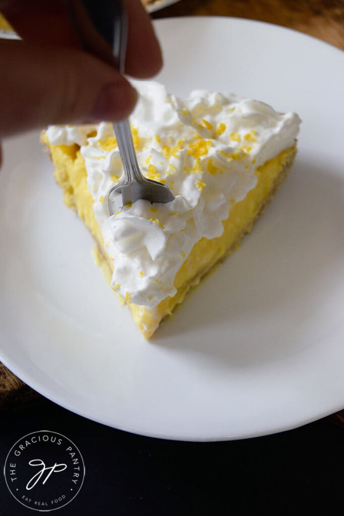 A fork being inserted into a single slice of lemon cream pie.