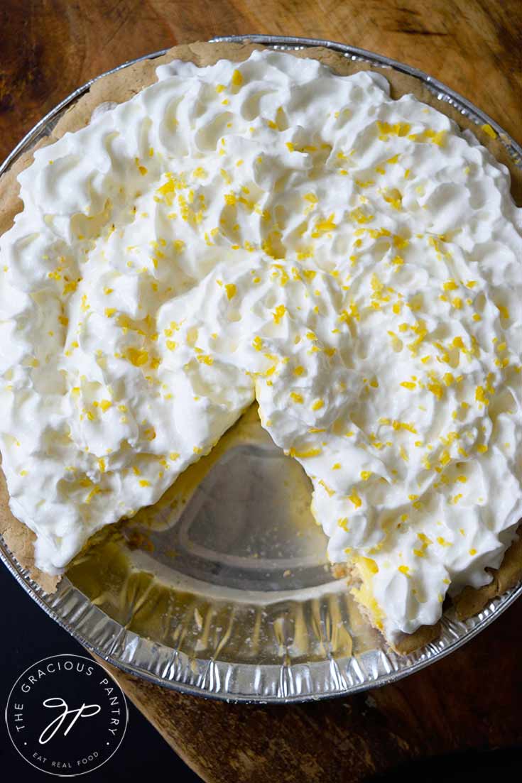 An overhead view looking down on a whole lemon cream pie with a one slice removed.
