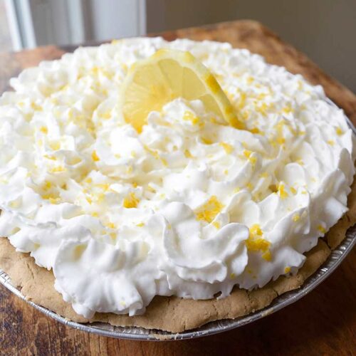 A side view of a whole lemon cream pie garnished with fresh lemon zest and a lemon slice.