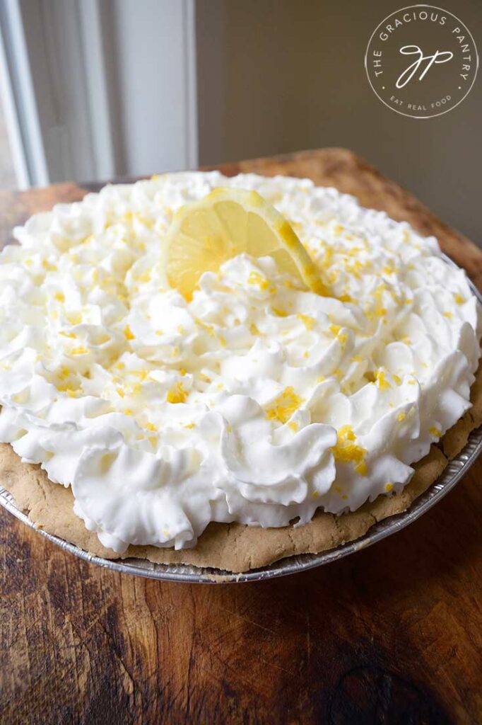 A side view of a whole lemon cream pie garnished with fresh lemon zest and a lemon slice.