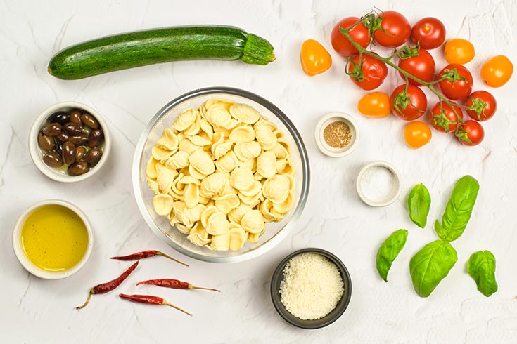 Orecchiette Pasta Salad Recipe ingredients gathered in individual bowls on a white surface.