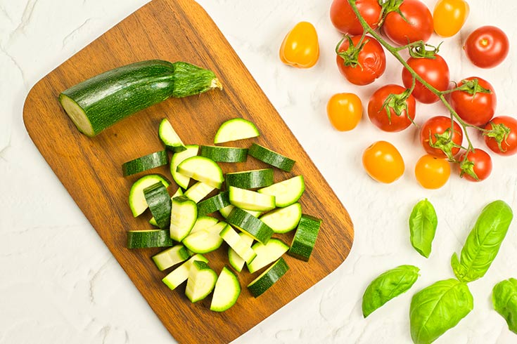 A raw zucchini cut into pieces and laying on a cutting board.