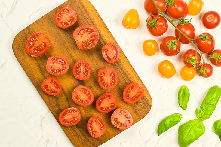 Cherry tomatoes cut in half and laying on a wood cutting board.