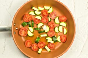 Raw tomatoes and zucchini sitting in a skillet.
