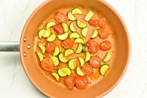 Roasted zucchini and tomatoes cooking in a skillet.