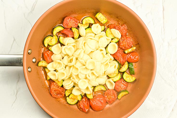 Orecchiette Pasta added to vegetables in a skillet.