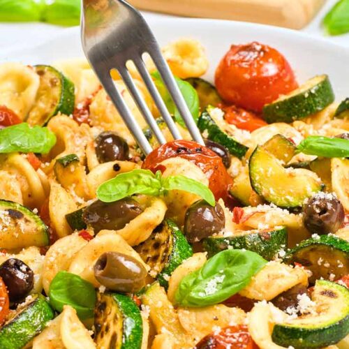 A fork sticks a tomato from a bowl of Orecchiette Pasta Salad.