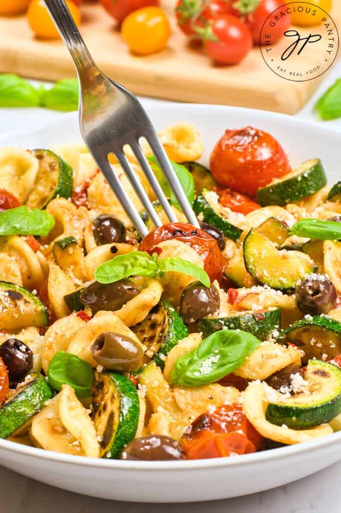 A fork sticks a tomato from a bowl of Orecchiette Pasta Salad.