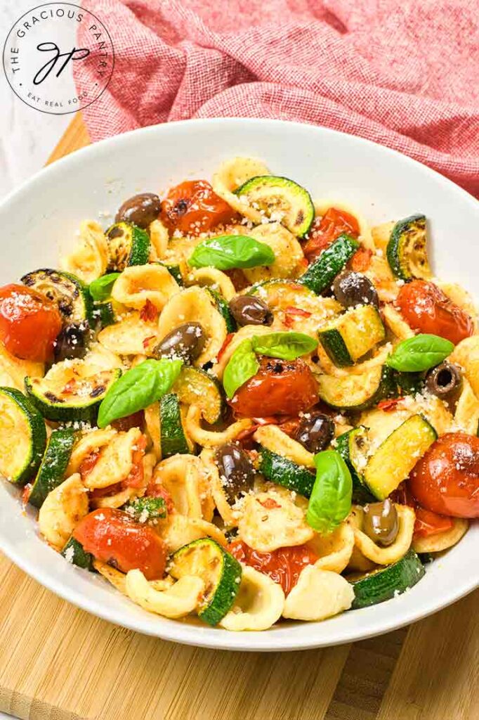 An overhead view of a white bowl filled with Orecchiette Pasta Salad sitting on a cutting board.