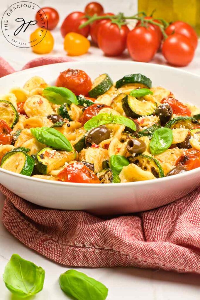 A white bowl filled with Orecchiette Pasta Salad sits on a rustic red dish towel.