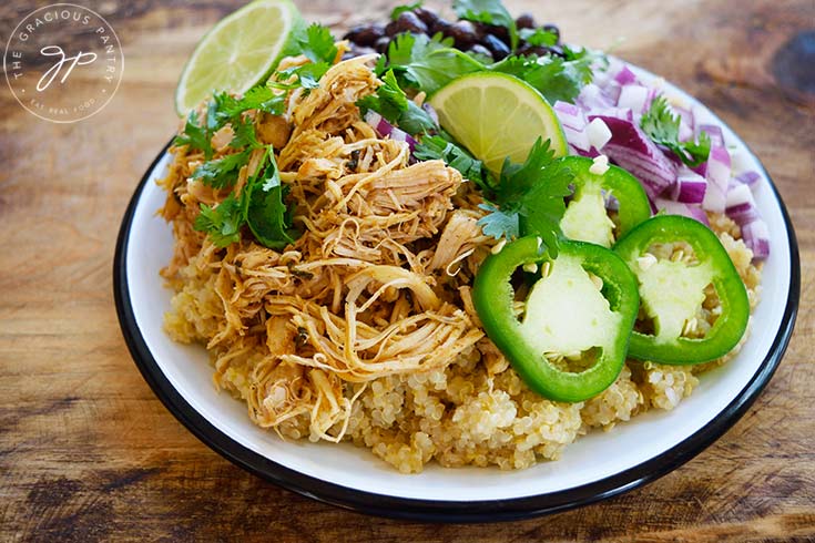 Slow Cooker Cilantro Lime Chicken served over quinoa and garnished with jalapeno pepper slices, lime slices, onions and black beans.