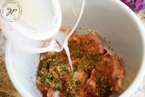 Pouring chicken broth into a slow cooker with chicken thighs and Slow Cooker Cilantro Lime Chicken sauce.