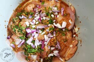 Onions sprinkled over chicken thighs in a slow cooker.