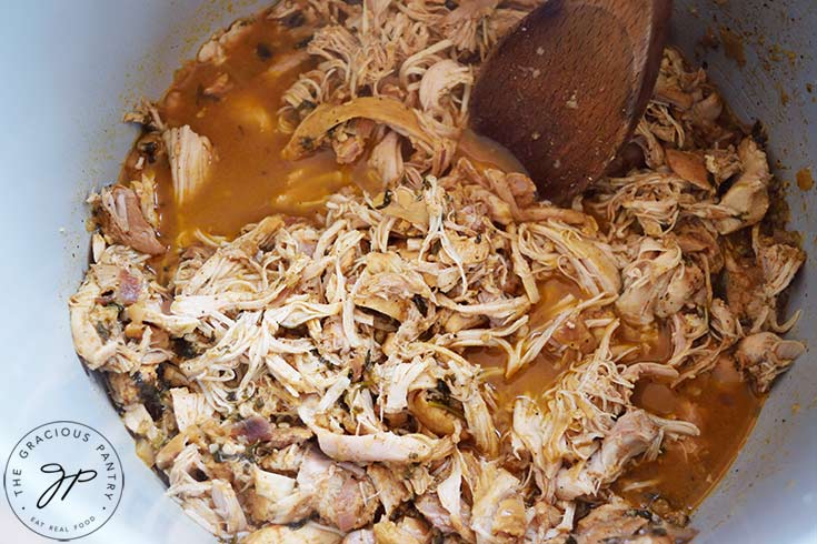 Slow Cooker Cilantro Lime Chicken, shredded with a wooden spoon, sitting in a slow cooker.