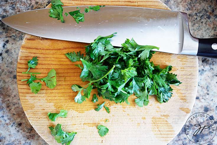 Chopped cilantro laying on a round, wood, cutting board.