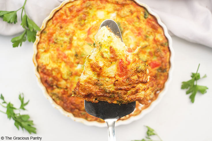 A spatula lifts a slice of Vegetable Breakfast Tart up out of a tart pan.