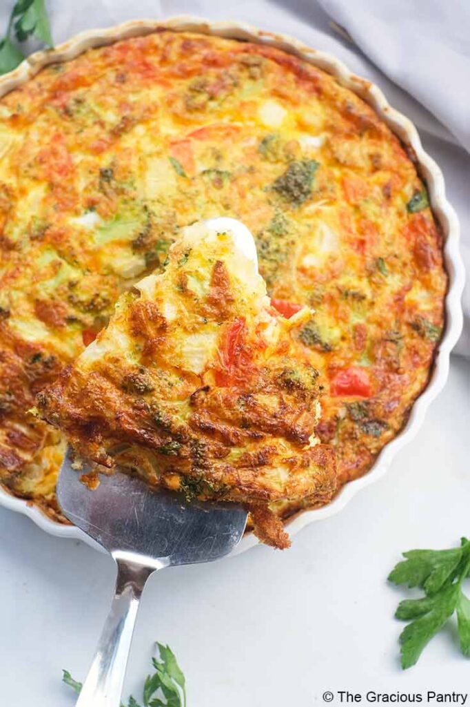 An overhead view of a metal spatula lifting a slice of Vegetable Breakfast Tart out of a tart pan.