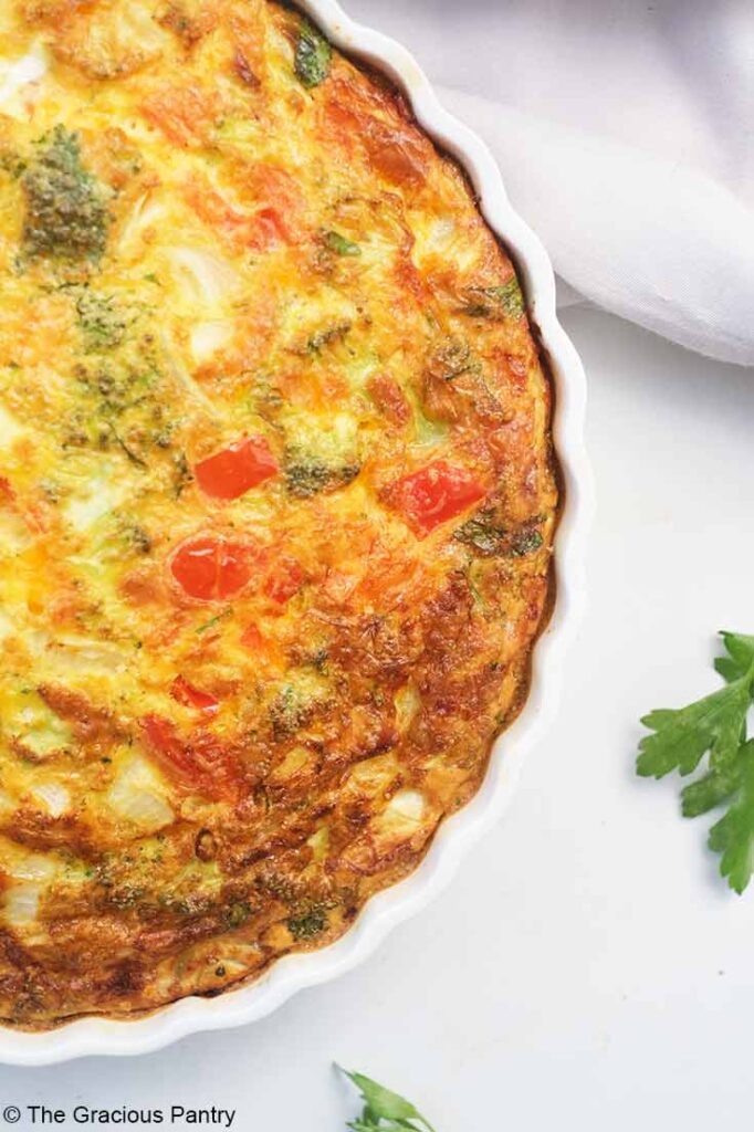 A partial, overhead view looking down on a Vegetable Breakfast Tart in a white ceramic tart pan.