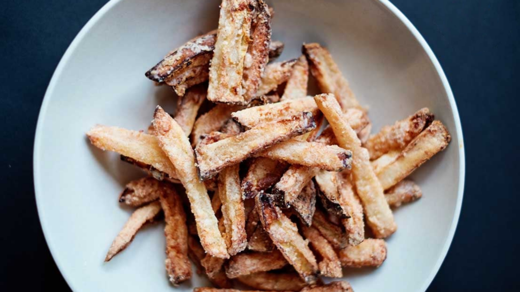 An overhead view of a white bowl holding a pile of apple fries.