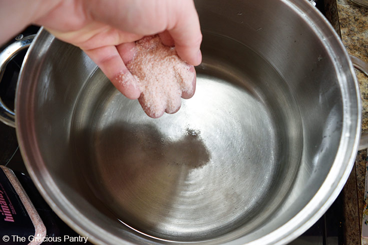 Adding salt to a large pot of water for salted pasta water.