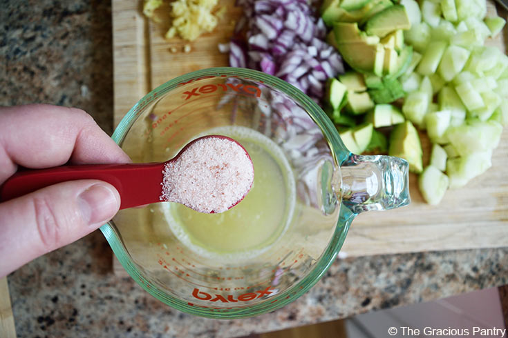 Adding salt to a measuring cup of dressing for this Avocado Pasta Salad Recipe.