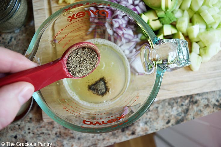 Adding pepper to a measuring cup of dressing for this Avocado Pasta Salad Recipe.
