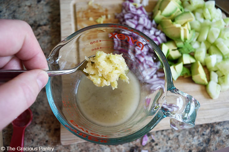 Adding pressed garlic to a measuring cup of dressing for this Avocado Pasta Salad Recipe.