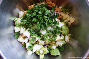 All the veggies and parsley added to pasta in a large metal mixing bowl for this Avocado Pasta Salad Recipe.