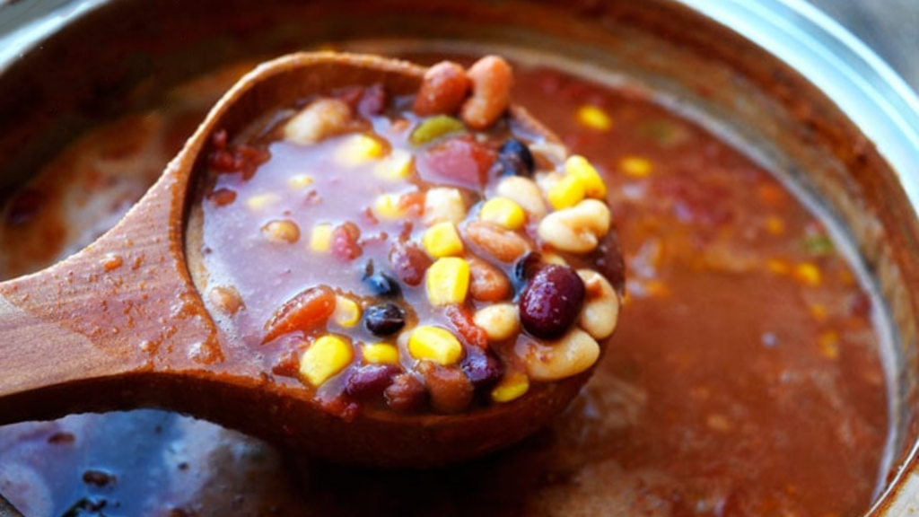 A wood ladle scoops up a scoop of bean chowder from a soup pot.