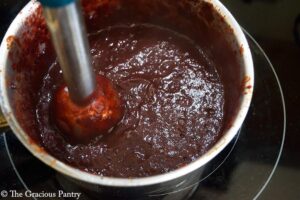 An immersion blender blends Blueberry BBQ Sauce in a pot.