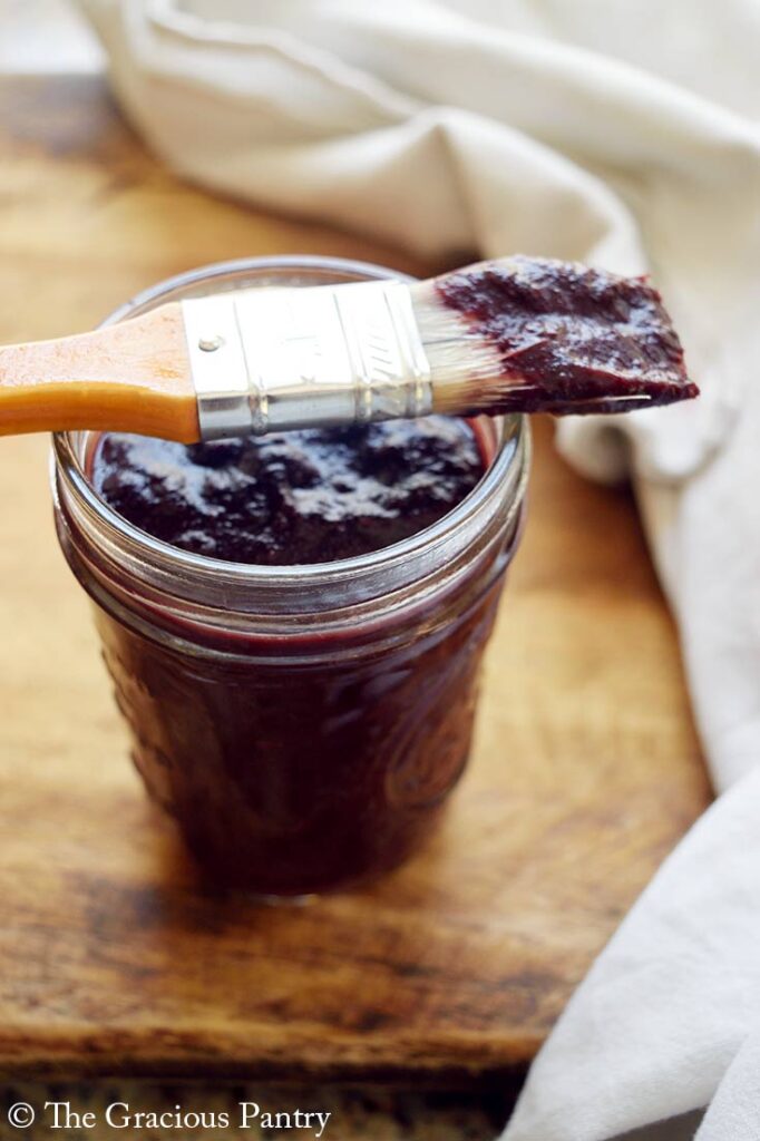 A basting brush which was dipped in Blueberry BBQ Sauce lays across the open jar of the sauce.