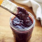 A basting brush dipped in Blueberry BBQ Sauce is held over the jar at an angle.