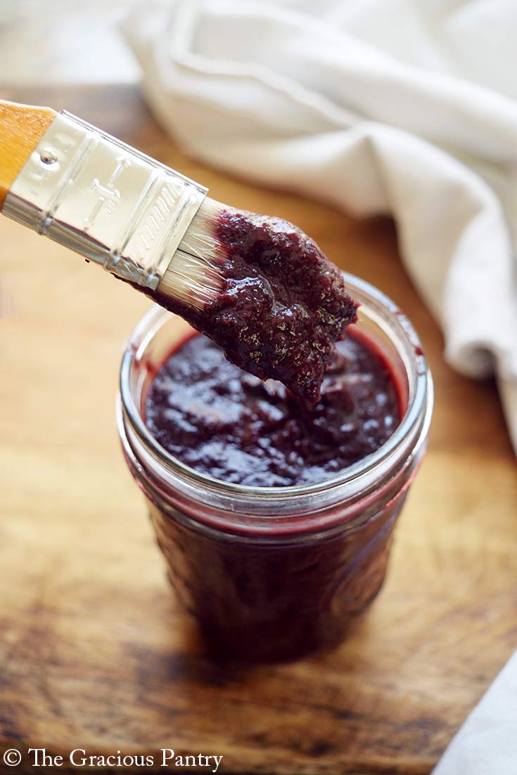 A basting brush dipped in Blueberry BBQ Sauce is held over the jar at an angle.