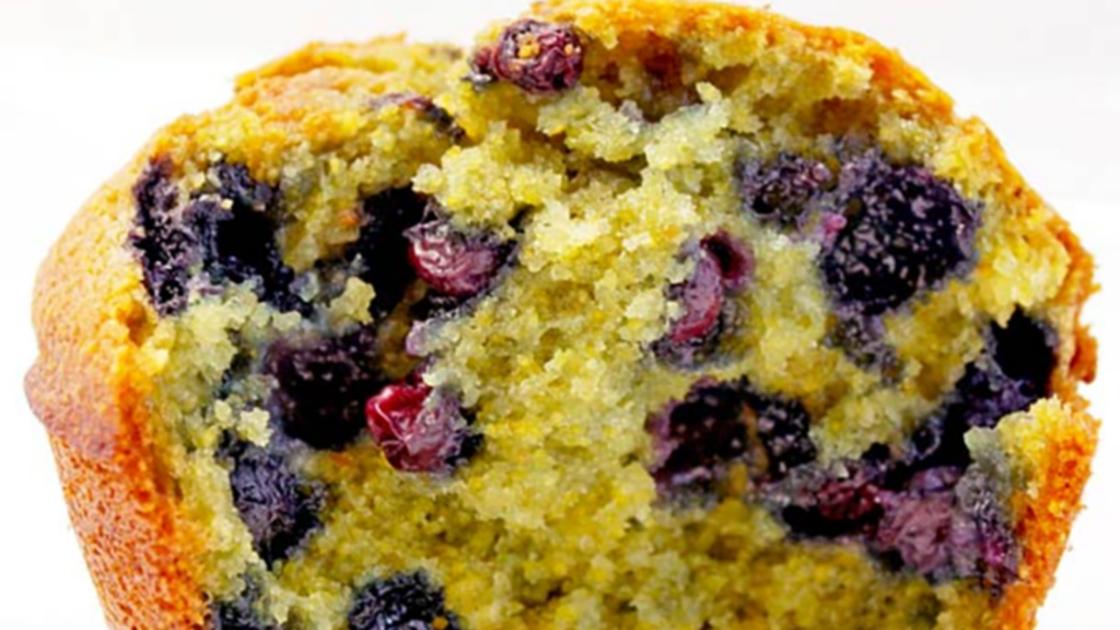 A closeup of a blueberry corn muffin that has a bite missing.