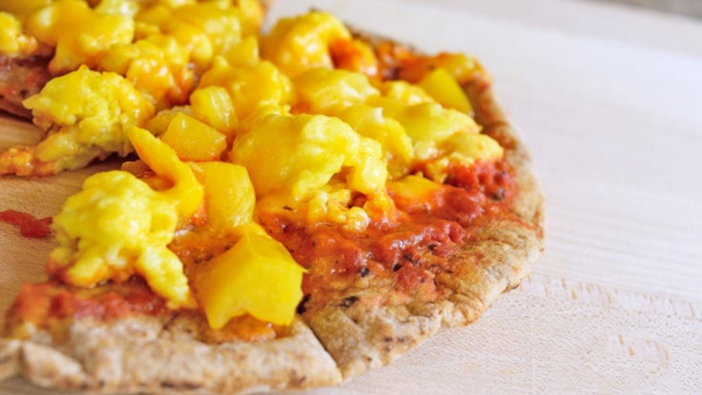 A pita bread with marinara and scrambled eggs lays on a wood surface.