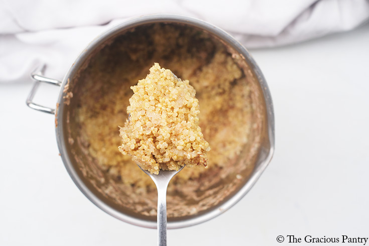 A spoon lifts some cooked Breakfast Quinoa our of a pot.