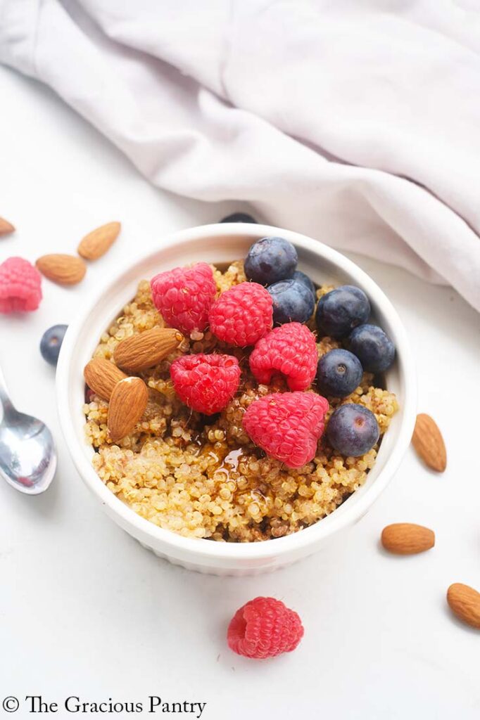 An overhead view of a white bowl filled with Breakfast Quinoa and topped with fresh raspberries and blueberries.