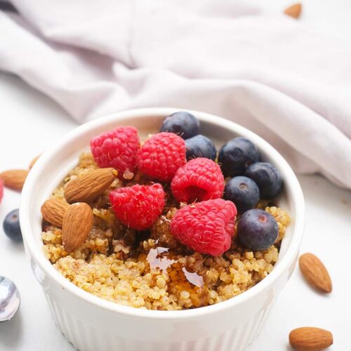 A side view of a white bowl filled with Breakfast Quinoa and topped with syrup and fresh berries.