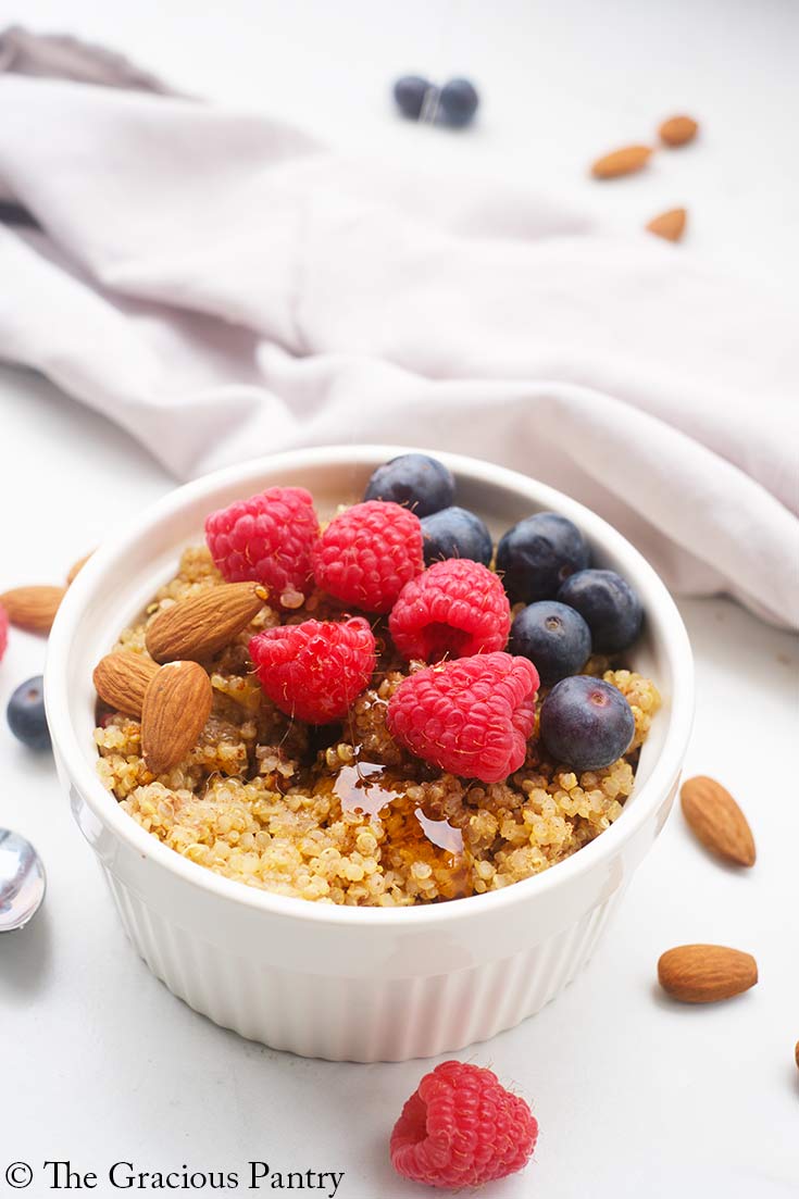 A side view of a white bowl filled with Breakfast Quinoa and topped with syrup and fresh berries.